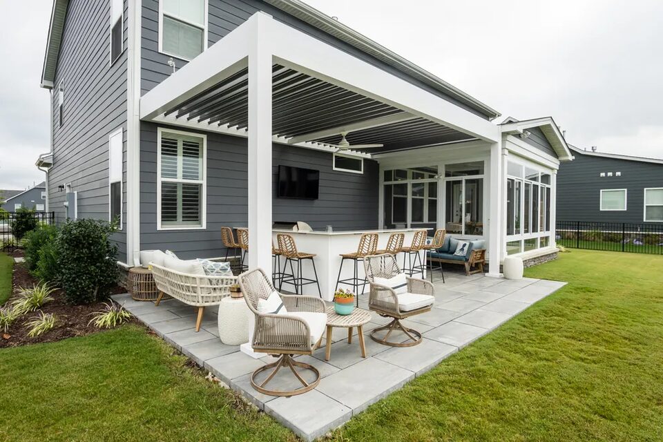 White louvered pergola over a patio beside a gray-sided home